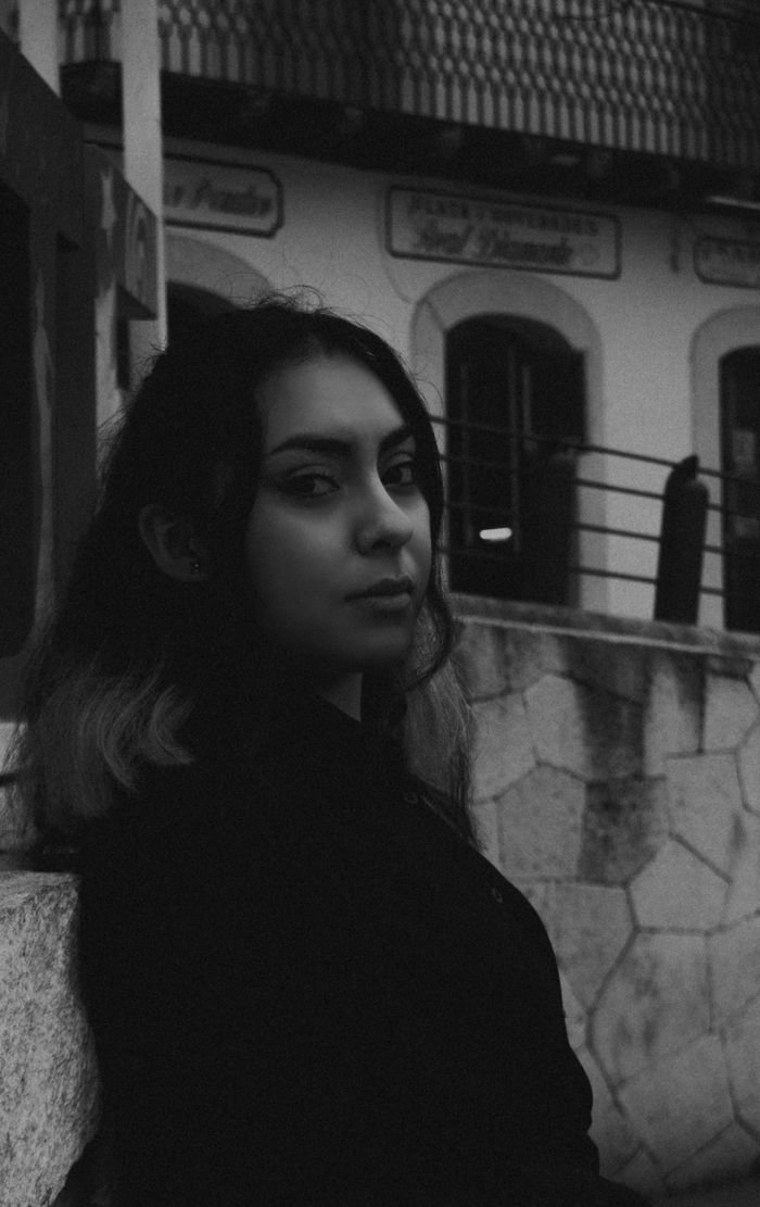 Artistic monochrome portrait of a young woman leaning against a stone wall.