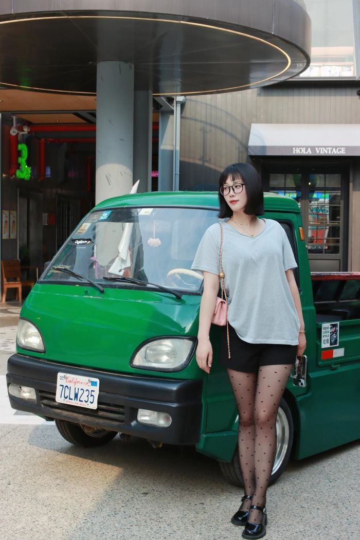 Modern woman posing with green mini truck at outdoor plaza in Nanjing, China.
